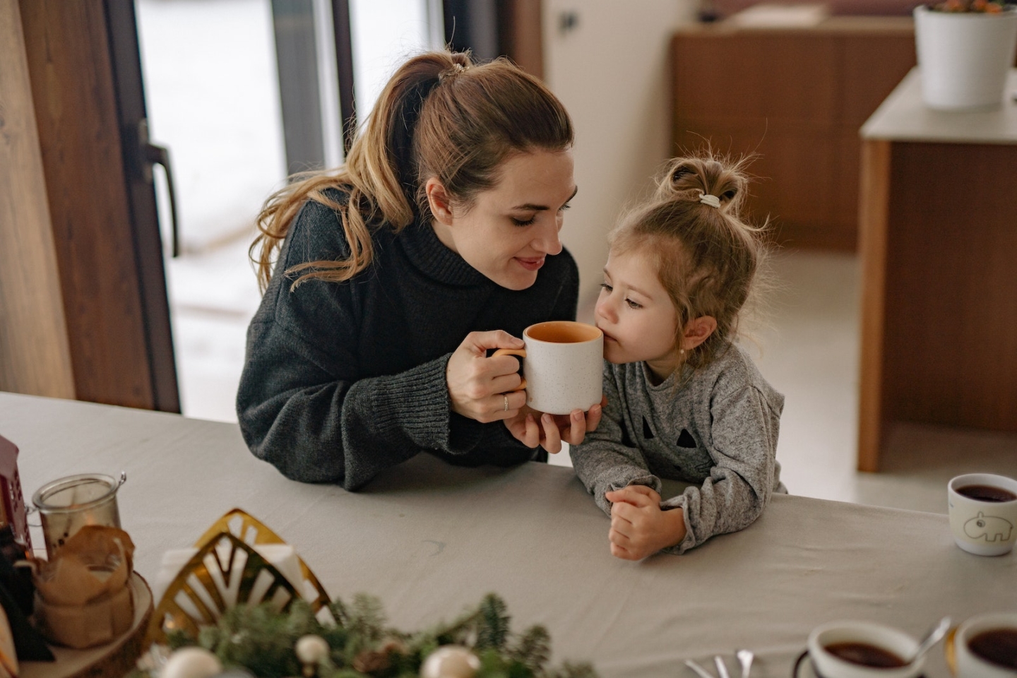 Woman Gives a Cup with Drink to Smell to a Girl Sitting Beside